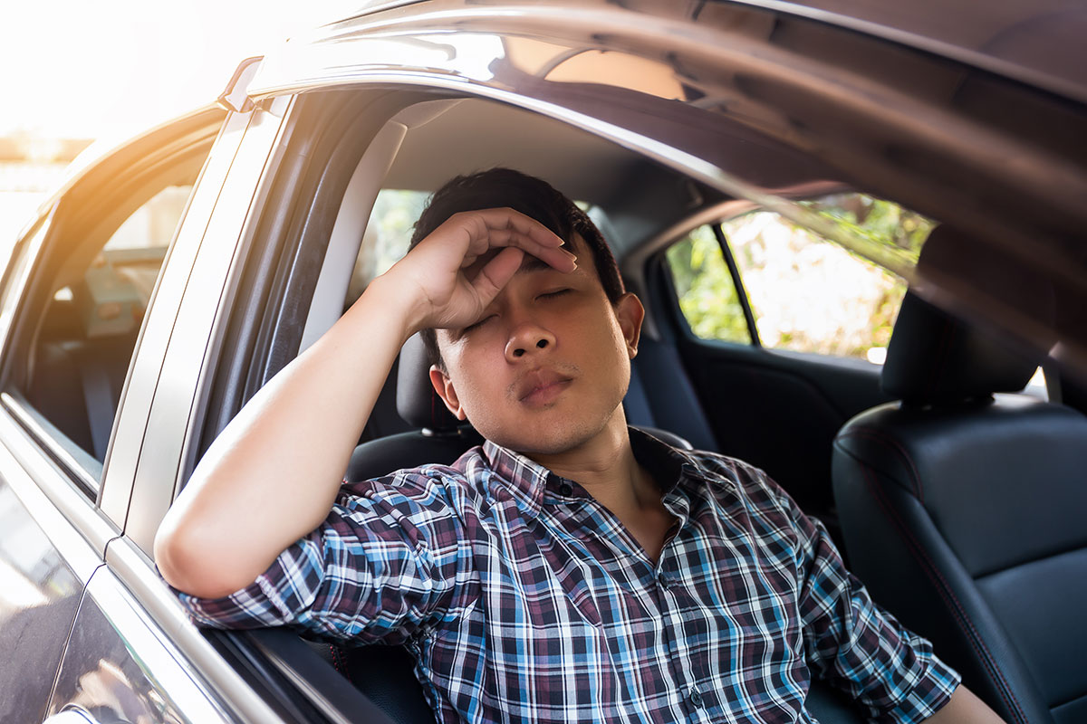 A man has his eyes closed and hand near his forehead as he suffers through an uncomfortable car ride