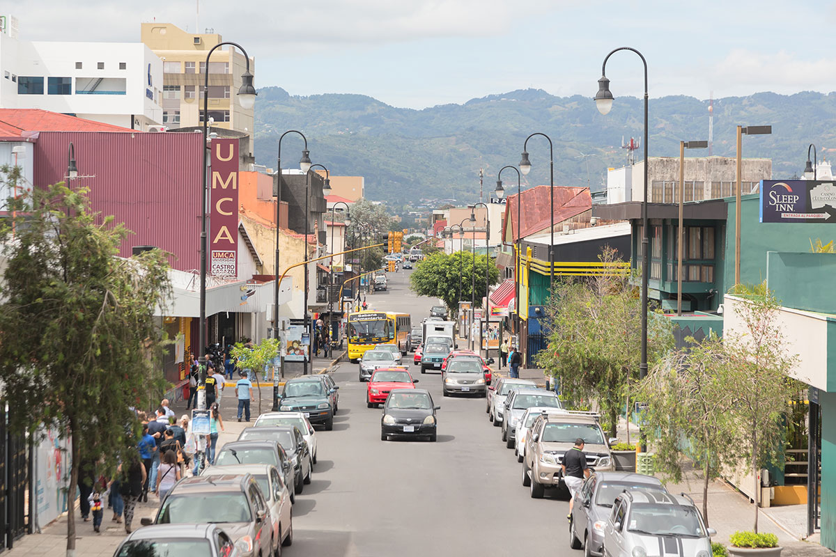Cars drive down, and line the streets of, downtown San José, Costa Rica