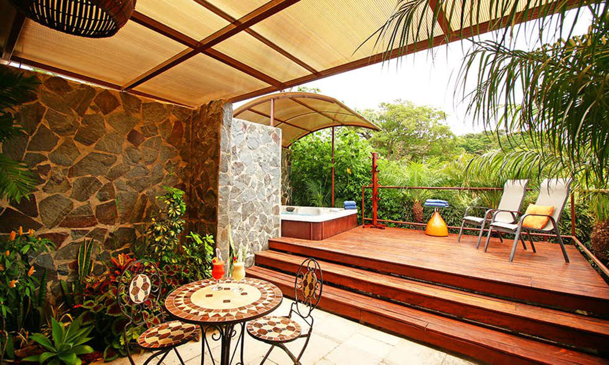 The outdoor area of Hotel Poco a Poco with bistro set and cocktails, and two lounge chairs on a deck near the Jacuzzi