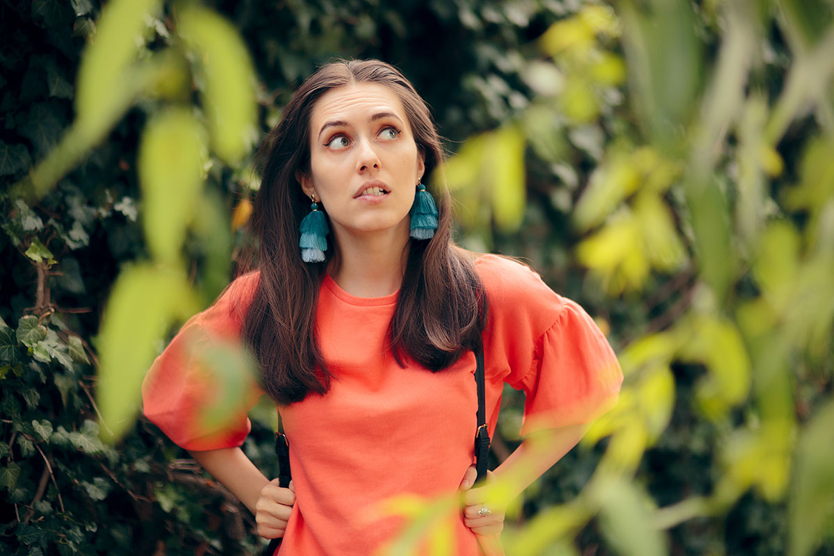 A woman in an orange top and green earrings ponders zip lines